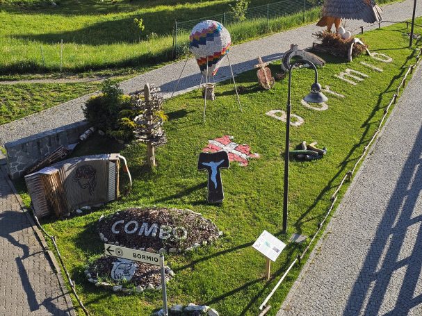 Liebevoll dekorierter Garten mit bunten Figuren und Wegweisern an einer Straße in den italienischen Alpen Liebevoll dekorierter Garten mit bunten Figuren und Wegweisern an einer Straße in den italienischen Alpen