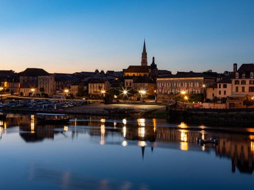 Abendliche Stadtansicht mit beleuchteten Gebäuden und Spiegelungen im Wasser in Bergerac an der Dordogne
