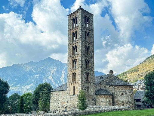 Historische romanische Steinkirche mit hohem Glockenturm vor der Bergkulisse der Pyrenäen
