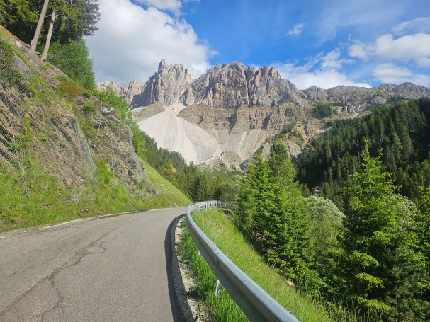 Kurvenreiche Bergstraße durch die Dolomiten Kurvenreiche Bergstraße mit Leitplanke, grünen Wäldern und imposanten Felswänden in den Dolomiten