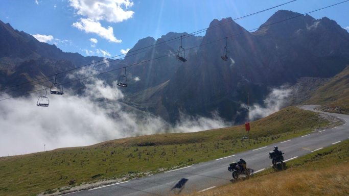 Motorräder auf einer Bergstraße vor steilen Felsgipfeln und aufziehenden Wolken in den Pyrenäen